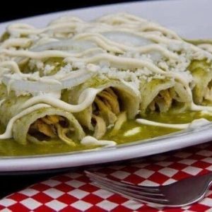 Plato de enchiladas verdes rellenas de pollo, cubiertas con salsa verde, crema y queso sobre un mantel rojo a cuadros.