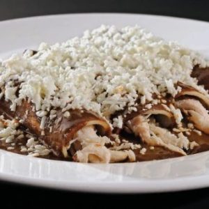 Plato de enmoladas rellenas de pollo y cubiertas con abundante queso fresco rallado sobre una deliciosa salsa de mole.